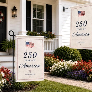 Peut inclure: Deux drapeaux de jardin rectangulaires avec le drapeau américain et le texte "250 YEARS OF AMERICA 1776-2026" en bleu marine. Les drapeaux sont beiges avec une bordure rouge, affichés sur des supports en métal noir.