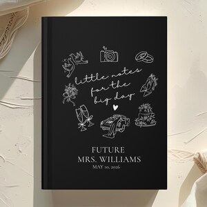 May include: A black journal with white line art illustrations of wedding-related icons, including doves, a camera, rings, and a cake. The text "little notes for the big day" is written in cursive. The journal is personalized with the text "FUTURE MRS. WILLIAMS MAY 10, 2026."