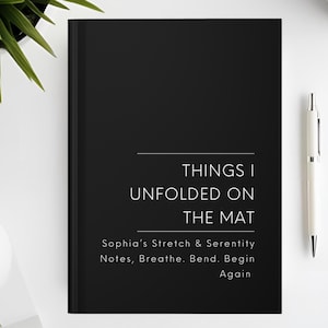 以下が含まれることがあります： 「THINGS I UNFOLDED ON THE MAT」の文字が白で書かれた黒いジャーナル。タイトルの下には「Sophia's Stretch & Serenity Notes, Breathe. Bend. Begin Again」という言葉があります。右側には白いペンが置かれています。