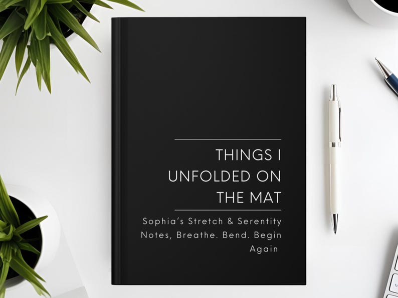 以下が含まれることがあります： 「THINGS I UNFOLDED ON THE MAT」の文字が白で書かれた黒いジャーナル。タイトルの下には「Sophia's Stretch & Serenity Notes, Breathe. Bend. Begin Again」という言葉があります。右側には白いペンが置かれています。