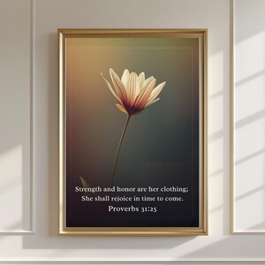 May include: A framed print showing a close-up of a white and red flower against a dark background. The gold frame surrounds the image, which includes the text "Strength and honor are her clothing; She shall rejoice in time to come. Proverbs 31:25."