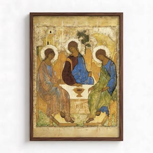 May include: A framed religious icon print depicting three winged figures seated around a table with a central chalice. The figures wear flowing robes in shades of blue, green, and deep red against a gold background, all enclosed in a dark wood frame.