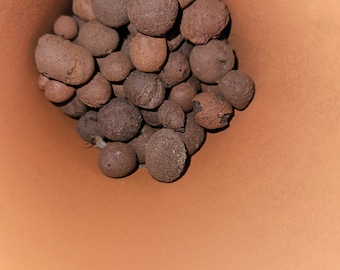 May include: A close-up view of the inside of a terracotta pot filled with brown clay pebbles.