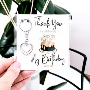 May include: A keychain with a silver heart charm attached to a card that says "Thank You For celebrating My Birthday With Me". The card features a gold and black birthday cake illustration.