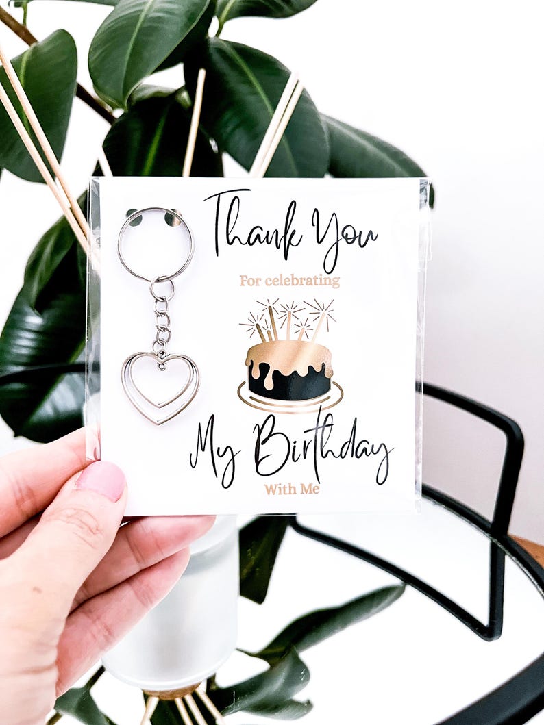 May include: A keychain with a silver heart charm attached to a card that says "Thank You For celebrating My Birthday With Me". The card features a gold and black birthday cake illustration.