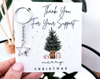 May include: A Christmas card with the message "Thank You For Your Support" and "merry CHRISTMAS". A silver star keyring is attached. The card design includes a Christmas tree and wrapped presents.
