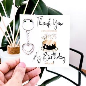 May include: A silver heart-shaped keychain with a card that says "Thank You For celebrating My Birthday With Me". The card features a black and gold birthday cake illustration.