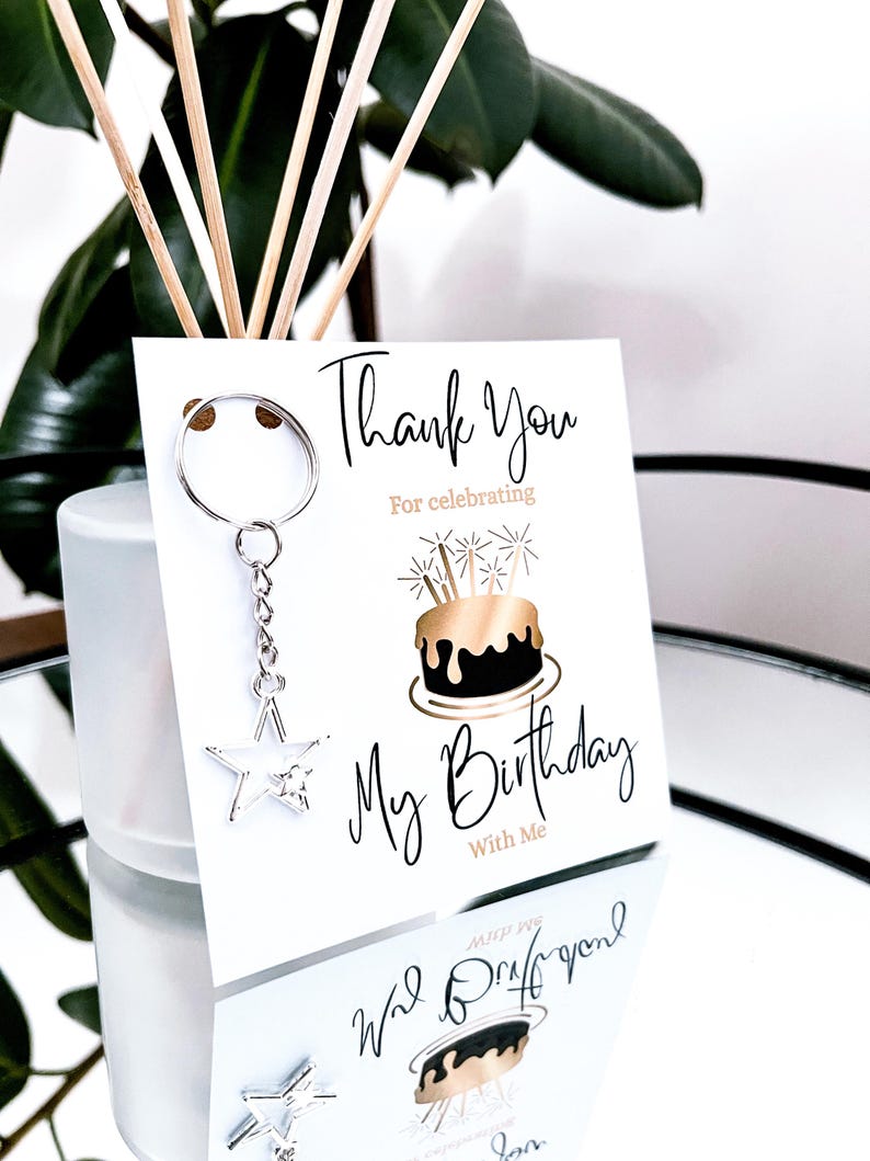 May include: A white birthday thank you card with the text "Thank You For celebrating My Birthday With Me". A silver star keychain hangs from the card. The card features a gold and black cake illustration.