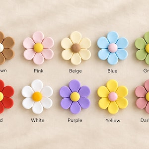 May include: Ten flower-shaped buttons arranged in two rows. Each button has five petals and a central circular accent. Colors include brown, pink, beige, blue, green, red, white, purple, yellow, and dark pink, with labels below each.