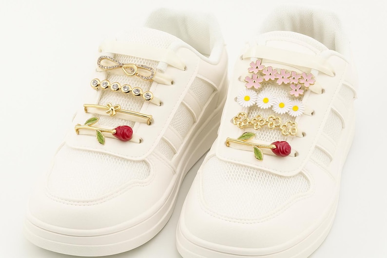 White sneaker decorated with various gold, crystal, and floral shoelace clips arranged horizontally across the laces.