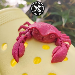 May include: A bright yellow pair of clogs with a red plastic crab charm attached. The crab has a detailed design and is positioned on top of the clog.