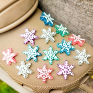 Op de afbeelding: Een close-up van een bruine schoen met een verscheidenheid aan kleurrijke sneeuwvlokcharms eraan bevestigd. De charms zijn gemaakt van helder plastic met witte sneeuwvlokontwerpen en hebben een glinsterende afwerking.