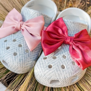 Peut inclure: Deux paires de sabots à motifs gris et blancs avec un nœud rose sur l'un et un nœud rouge sur l'autre.