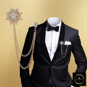 Puede incluir: Una chaqueta de esmoquin negra con camisa blanca, pajarita negra y pañuelo de bolsillo blanco. Un broche dorado en forma de estrella con cristales transparentes y dos cadenas colgantes está prendido en la solapa, con un accesorio a juego.