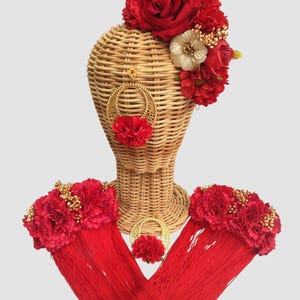 Puede incluir: Conjunto de tocado floral rojo, collar y pulseras con detalles dorados. El conjunto incluye una corona de flores, un collar con un colgante y dos pulseras.