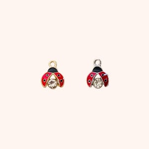 May include: Two ladybug charms, one gold-toned and one silver-toned, each with red enamel wings, black heads, and clear crystal bodies. The ladybugs have small black spots on their wings and are designed for jewelry making.