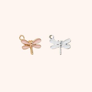 May include: Two dragonfly charms, one gold-toned with pink wings, the other silver-toned with white wings. Both charms have a loop for attaching to jewelry. The dragonfly charms are small and delicate.