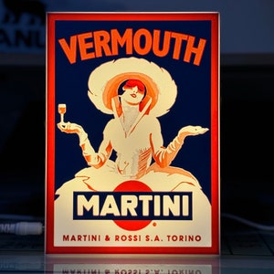 Puede incluir: Un anuncio vintage de Martini & Rossi Vermouth. El anuncio presenta a una mujer con un sombrero blanco y un vestido sosteniendo una copa de vermouth. El texto del anuncio dice "Vermouth Martini & Rossi S.A. Torino".