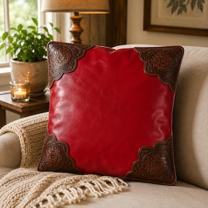 May include: A square throw pillow featuring a smooth, vibrant red center panel contrasted by dark brown, intricately embossed leather-like corner accents that display a detailed floral pattern, creating a distinct visual border on the cushion.