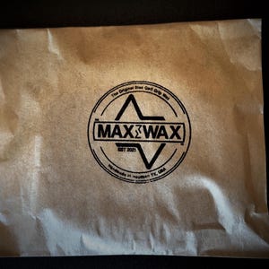 Puede incluir: Un sobre de papel marrón con un logotipo en blanco y negro que dice "Max Wax" y "The Original Disc Golf Grip Wax" con el texto "Est 2021" y "Handmade in Houston, TX, USA".