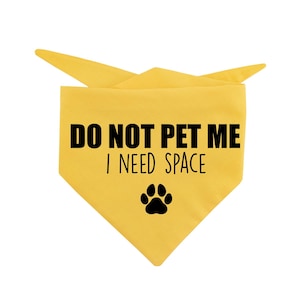 Può includere: Bandana gialla per cani con il testo nero "DO NOT PET ME I NEED SPACE" e un'impronta di zampa nera. La bandana è piegata a forma di triangolo.