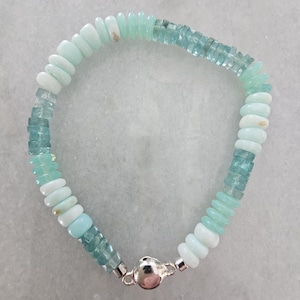 May include: A beaded bracelet featuring a mix of light blue and white gemstones. The bracelet has a silver clasp and is composed of various shapes and sizes of beads, creating a unique and eye-catching design. The bracelet is a piece of jewelry.