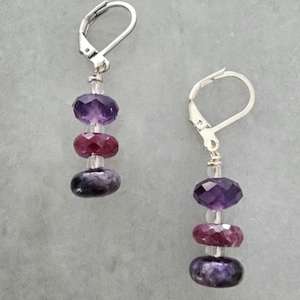 May include: A pair of dangle earrings featuring faceted purple and red gemstones. The earrings have a lever-back closure and are composed of three stacked stones in shades of purple and red, separated by clear beads.