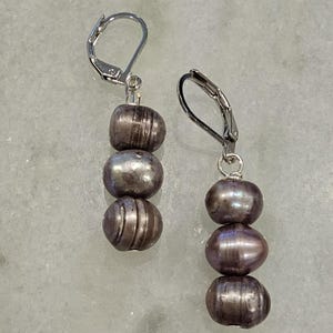 May include: A pair of silver dangle earrings with three gray pearls on each earring.