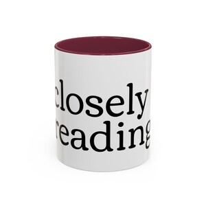 May include: White ceramic mug with a burgundy interior. The mug features the words "closely reading" in black, bold font. The mug is designed for hot or cold beverages.