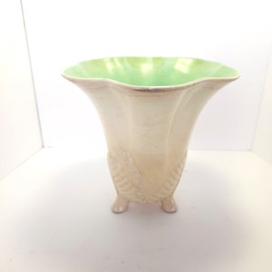May include: A white ceramic vase with a green glaze on the top. The vase has a scalloped rim and three feet.
