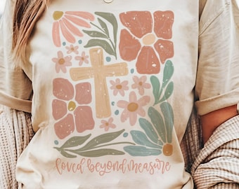 May include: A beige t-shirt with a floral design and a cross in the center. The text "loved beyond measure" is printed below the design.