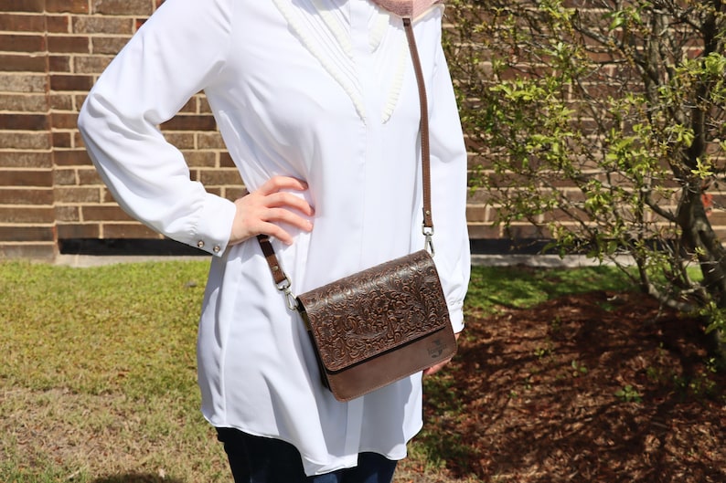 May include: A brown leather crossbody bag with an embossed floral design. The bag has a flap closure and a long adjustable strap.
