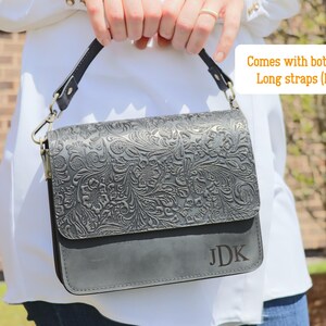 May include: A black leather handbag with an embossed floral design. The bag has a short strap and a long strap, and the initials "JDK" are embossed on the front.