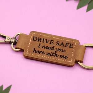 Puede incluir: Llavero de cuero marrón con un anillo de llave plateado y el texto "DRIVE SAFE I need you here with me".