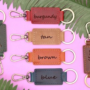 May include: Five leather keychains with metal rings and clasps. Each keychain has a different color and a word written on it: green, tan, brown, blue, and coffee.