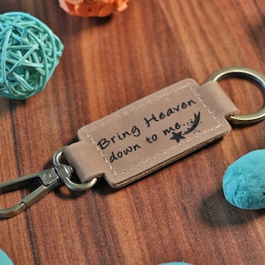 May include: A brown leather keychain with a silver metal clasp and a ring. The leather tag has the text "Bring Heaven down to me" with a star and a shooting star.