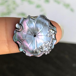 Könnte beinhalten: Schwarzer, irisierender Lotusblütenanhänger mit filigranen Details. Der Anhänger hat ein zentrales Loch und ein florales Design. Der Anhänger hat einen Durchmesser von etwa 3,8 cm.