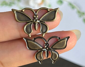 May include: Two antique gold-toned metal butterfly charms. The larger butterfly charm is slightly larger than the smaller butterfly charm.