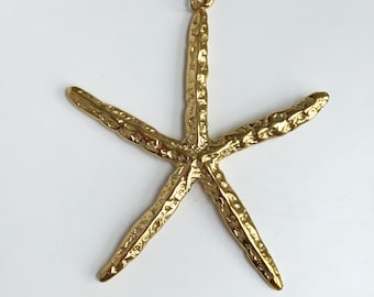 May include: A gold-coloured starfish pendant with a textured surface. The starfish has five arms and a small loop at the top for hanging. The pendant is set against a white background.