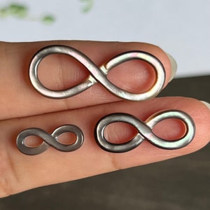 May include: Three infinity symbol charms made of iridescent mother of pearl. The charms are different sizes, with the largest charm being about 2 inches long.