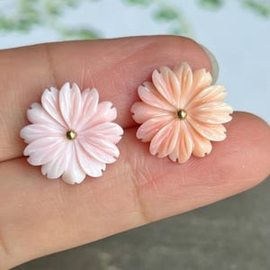 May include: Two pink coral flower earrings with gold centers. The earrings are carved in a delicate floral design.