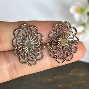 以下が含まれることがあります： 円形の穴が空いた、アンティークゴールドの金属製のフィリグリーの花の形をした装飾が2つあります。