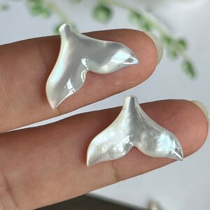 以下が含まれることがあります： 白虹色の真珠母貝のクジラの尾のチャーム2個。チャームはクジラの尾の形をしており、真珠のような仕上げになっています。