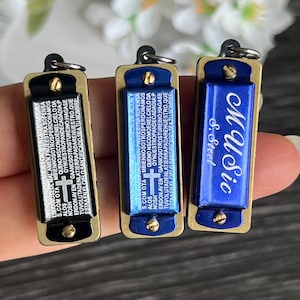 May include: Three small harmonicas with gold trim. The harmonicas are black, blue, and gold. The black harmonica has a religious inscription in Spanish. The blue harmonica has the text "123188 SW" on it.