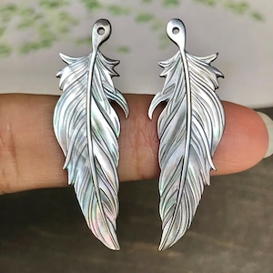 May include: Two silver feather pendants. Each pendant has a loop at the top for hanging and detailed feather vein patterns. The pendants are approximately 7.6 cm long.