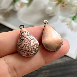May include: Two copper-toned teardrop-shaped locket pendants. One pendant features an engraved floral design, while the other is plain.