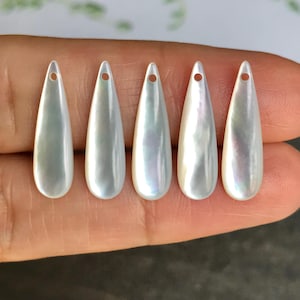 May include: Five pearlescent teardrop-shaped pendants with a hole at the top for stringing. The pendants have a lustrous, iridescent sheen, reflecting shades of white, silver, and subtle hints of color. These pendants are ideal for jewelry making.