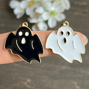 May include: Two gold-colored ghost charms, one black and one white, with white eyes and a black mouth. The charms are enamel-painted and have a shiny finish.