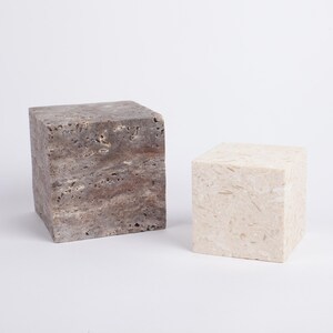 May include: Two square stone pedestals, one is a light brown color and the other is a light beige color.