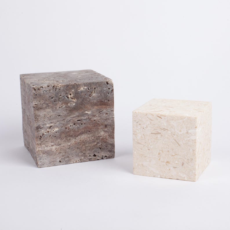 May include: Two square stone pedestals, one is a light brown color and the other is a light beige color.